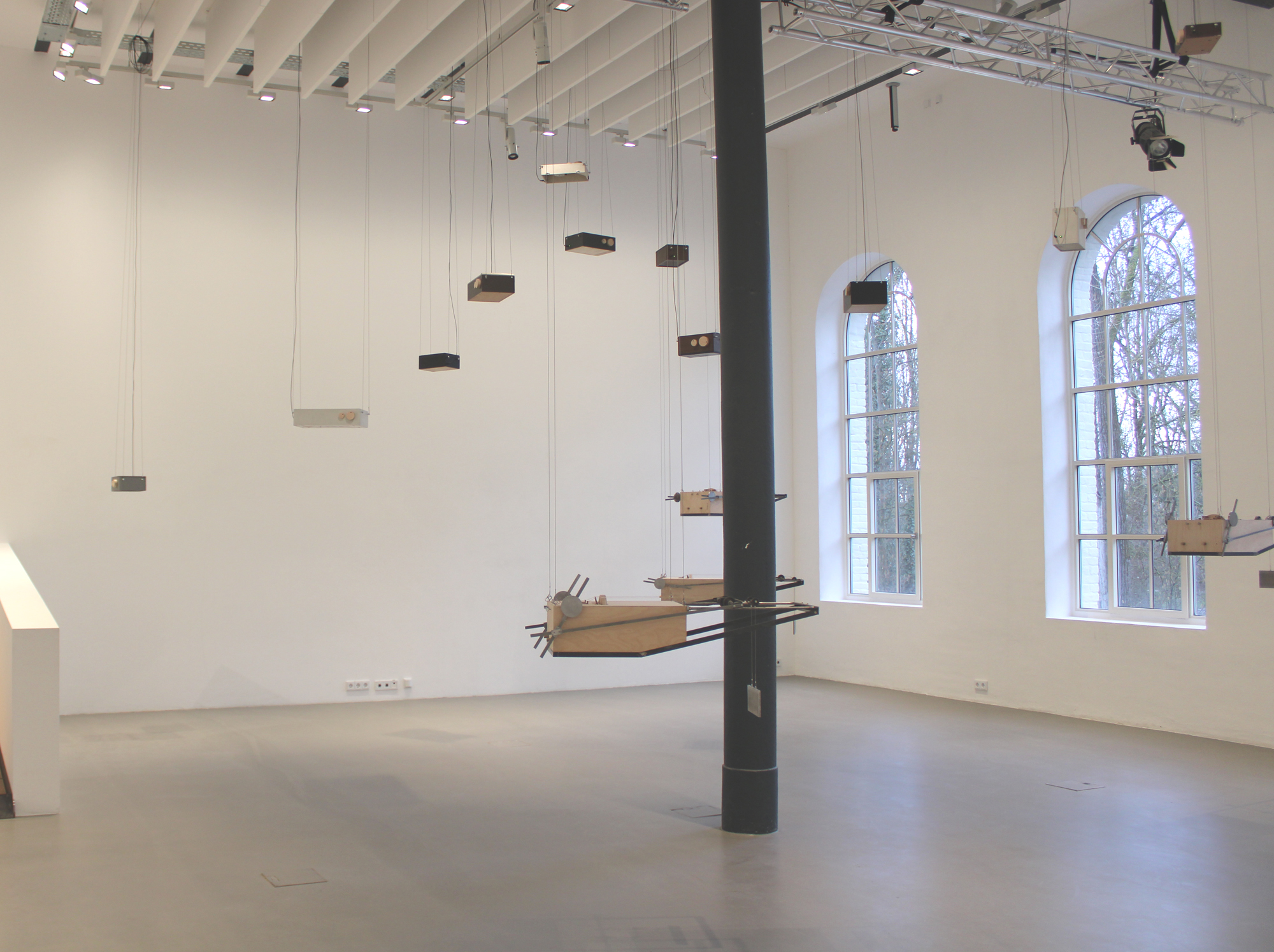 A photo of the exhibition 'Entering into the sound' showing a wide perspective of the main room, with tone generators and instrument sculptures hanging from the ceiling.